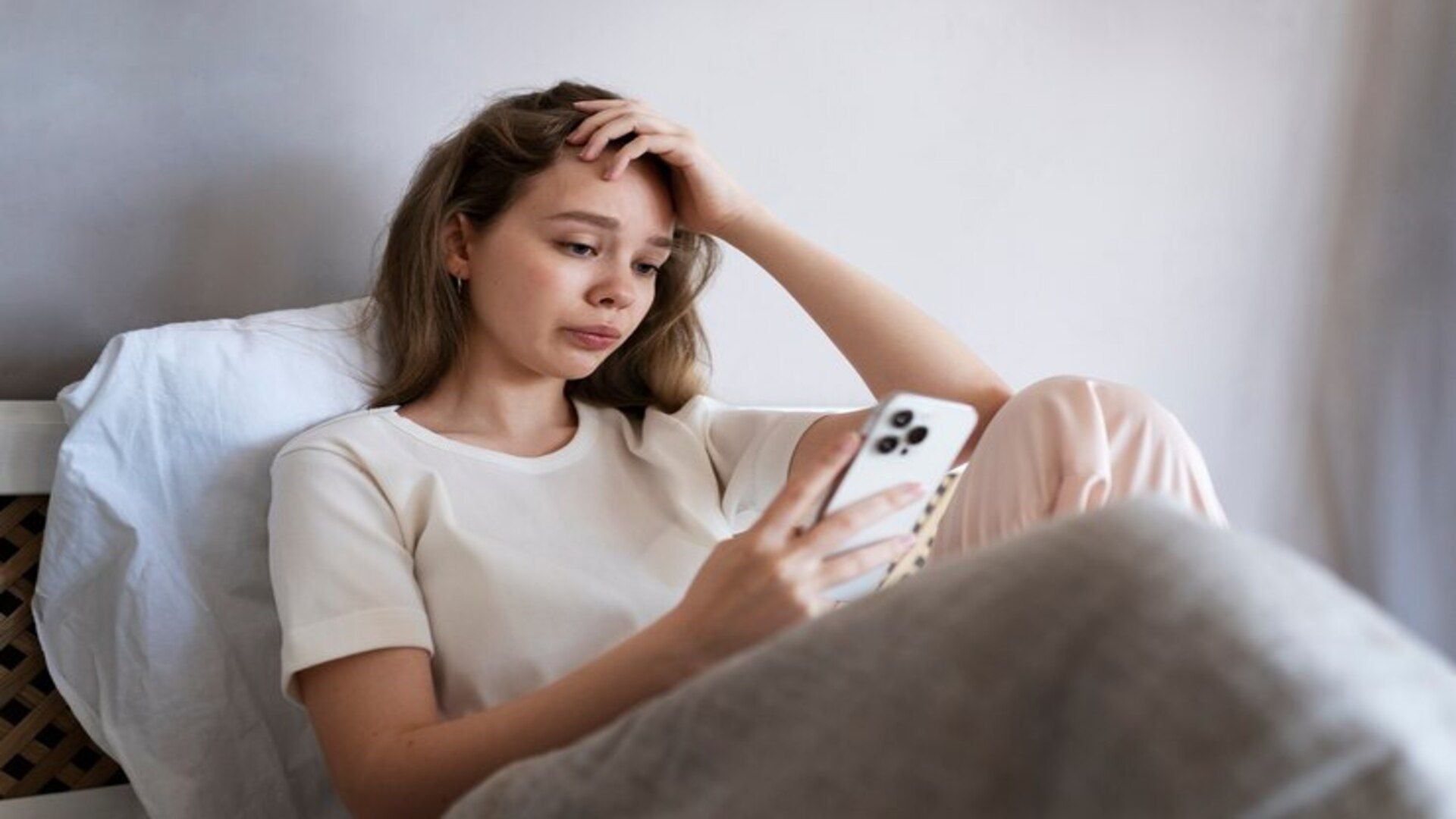 Mujer con ansiedad echada en su cama mirando su celular (Freepik)