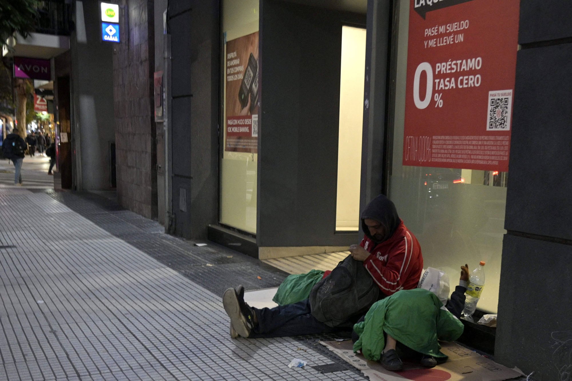 Un hombre con dos niños pide limosna en la puerta de un banco que ofrece préstamos a tasa del 0% en Buenos Aires