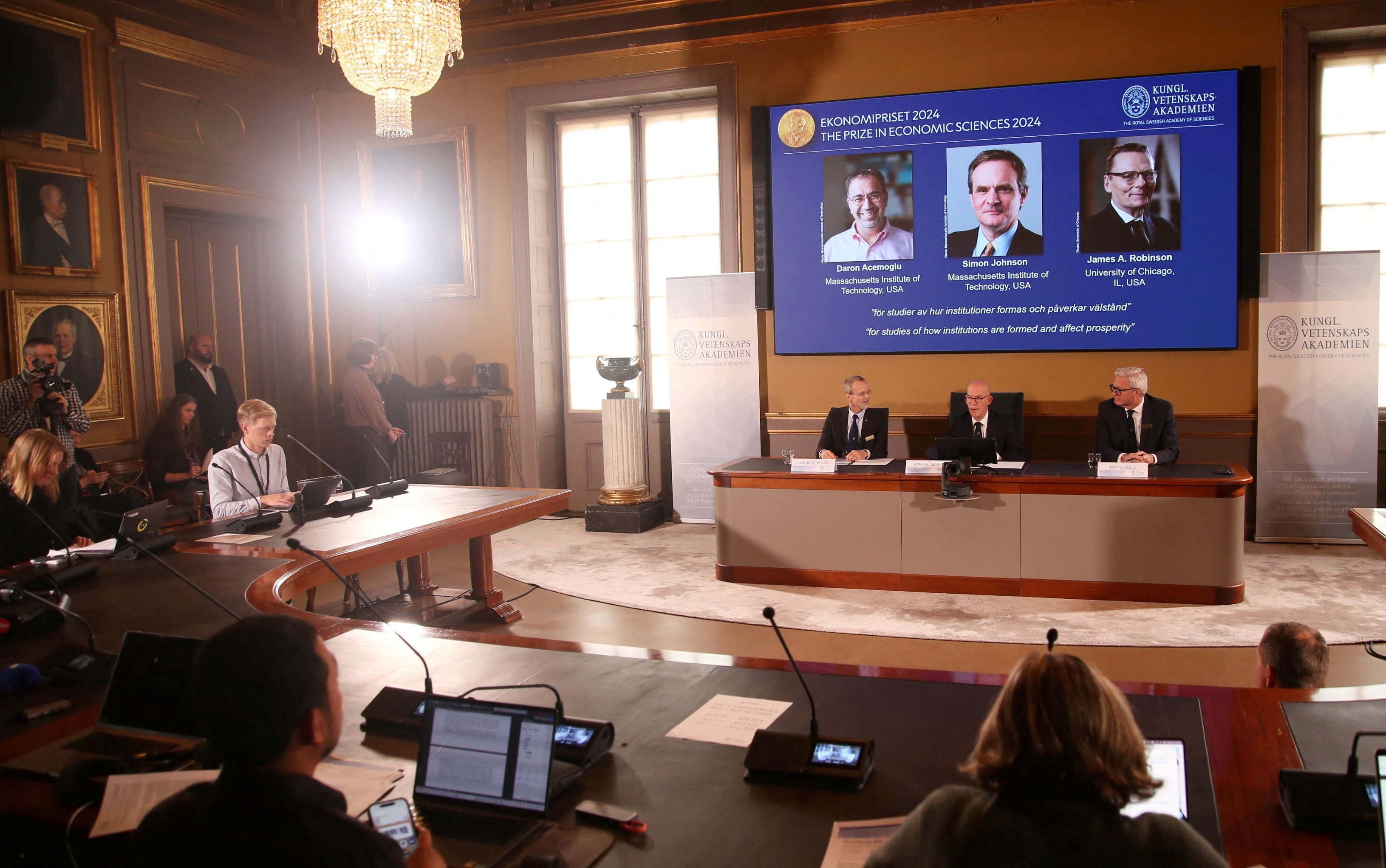 Una pantalla muestra a los galardonados (de izquierda a derecha) el turco-estadounidense Daron Acemoglu y los británico-estadounidenses Simon Johnson y James Robinson, ganadores del Premio del Banco de Suecia en Ciencias Económicas en Memoria de Alfred Nobel 2024, durante el anuncio realizado por la Real Academia de las Ciencias de Suecia en Estocolmo, Suecia (Reuters)